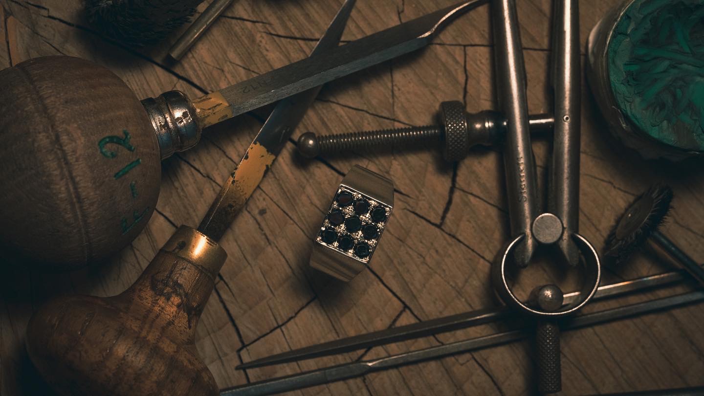 A finished signet ring set with black diamonds, among the tools that made it.